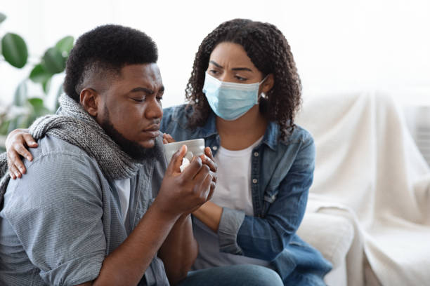 help1 Supportive African Wife Taking Care About Her Ill Husband At Home, Wearing Medical Mask Not To Get Sick, Closeup