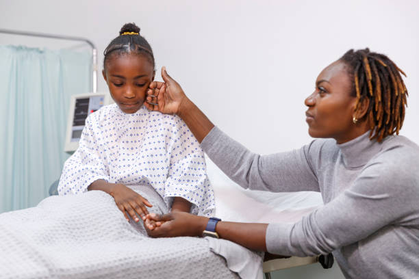 help5 A black preadolescent girl looks sad and nervous as she sits in a hospital bed. The child's loving mom is sitting next to the bed and is holding the girl's hand, providing support and encouragement.